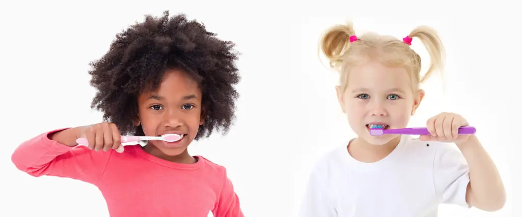 Little girl brushing teeth next to younger blonde girl against white background