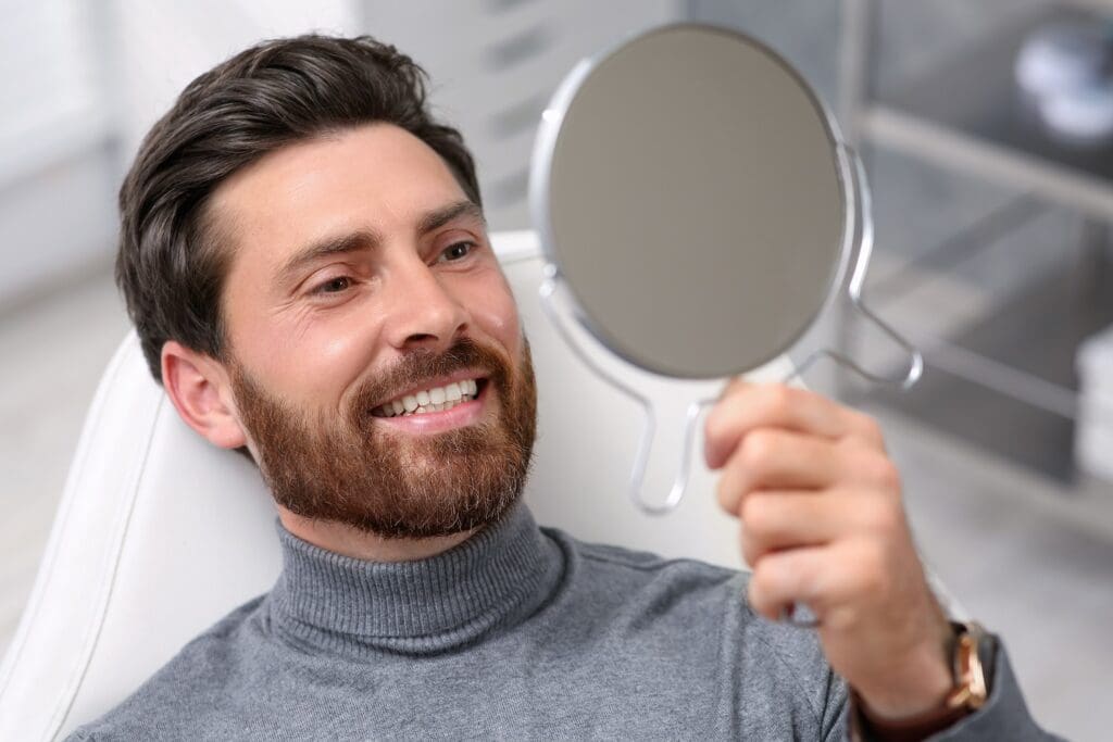 Smiling male patient holding dental mirror during orthodontic checkup