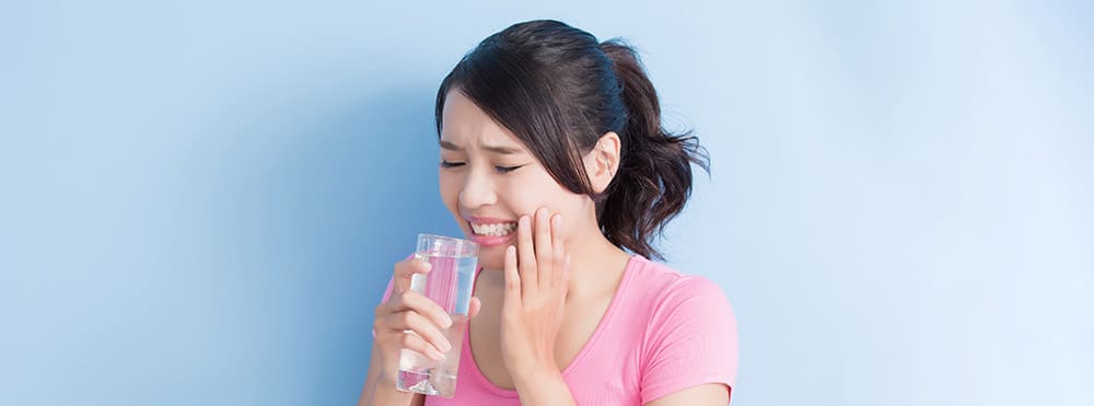 Young woman holding glass of water and smiling with hand on cheek against blue background